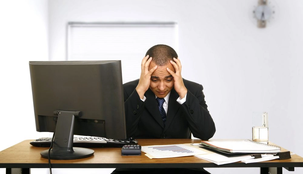 Stressed businessman in suit sitting at desk with financial documents and computer, holding his head in frustration. Why AI Financial Advisors Are Becoming Your Smart Money Guide in 2025
