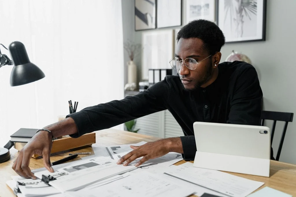 Person organizing financial documents at a desk with a tablet and office supplies in a modern workspace.